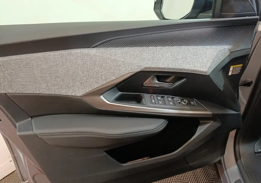 Vue intérieure côté gauche de la porte avant d’un Peugeot 5008 gris clair, avec garniture tissu et commandes électriques.