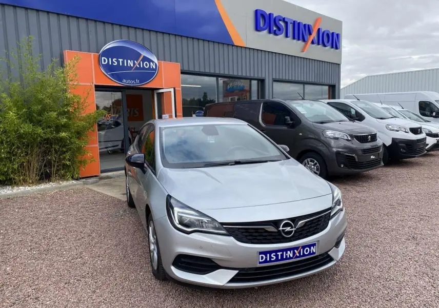 Opel Astra 1.2i Turbo gris argent vue 3/4 avant, avec calandre noire et phares LED, devant un garage Distinxion.