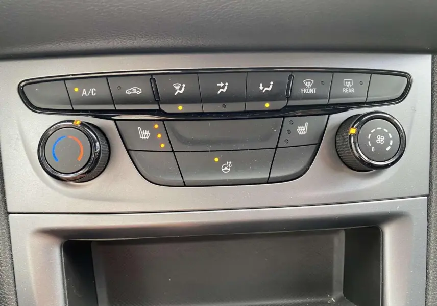 Gros plan sur la console centrale grise de l'Opel Astra 2021, avec commandes de climatisation et sièges chauffants allumés.