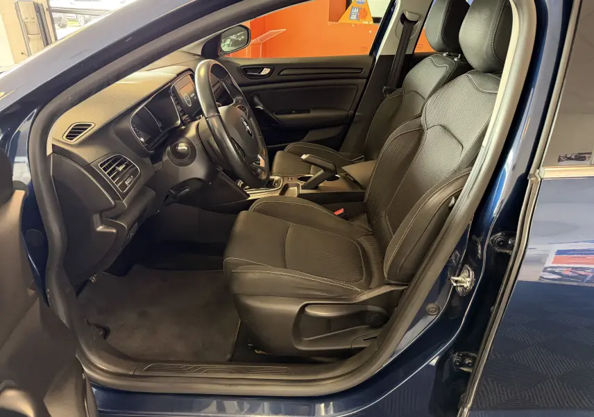 Vue intérieure côté conducteur d'une Renault Mégane bleu 2019, sièges noirs et tableau de bord moderne.