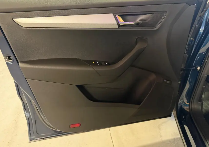 Vue rapprochée de la porte avant gauche d'une Skoda Karoq bleu 2023, avec garniture noire et insert chromé.