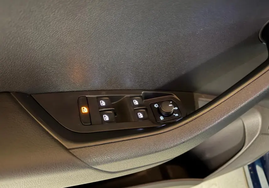 Gros plan sur les commandes de lève-vitres et rétroviseurs sur la porte côté conducteur d’un Skoda Karoq bleu 2023.