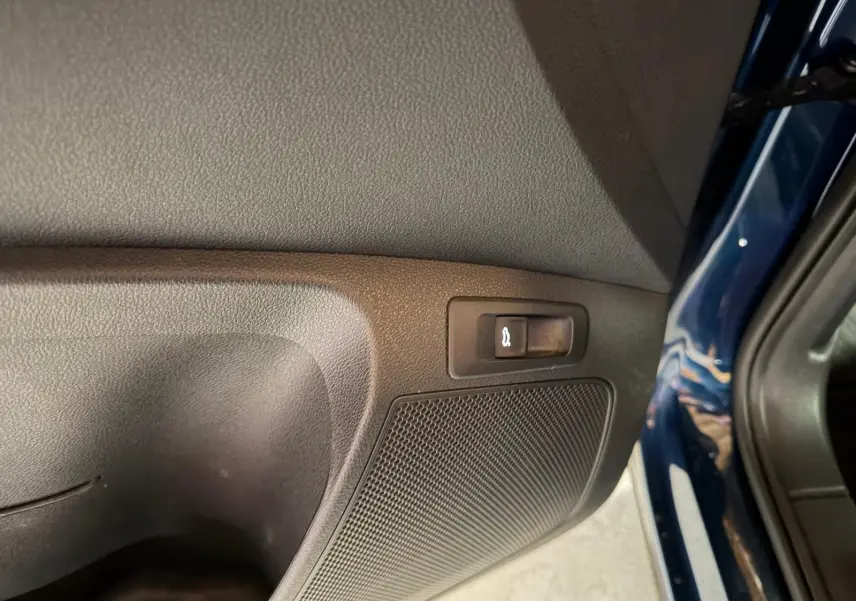Détail intérieur côté gauche du coffre d’un Skoda Karoq bleu 2023 avec bouton d’ouverture du hayon.
