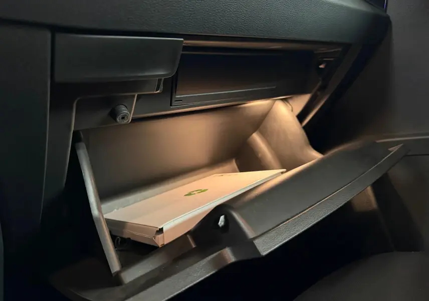 Gros plan sur la boîte à gants ouverte de la Skoda Karoq 2.0 TDI bleu, avec éclairage intérieur et document à l'intérieur.