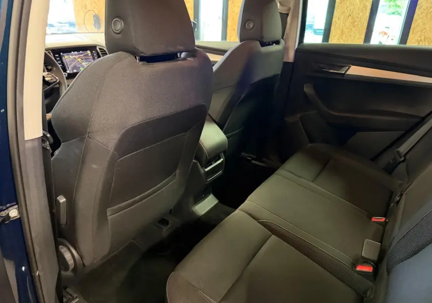 Vue intérieure arrière droite du Skoda Karoq bleu 2023, sièges tissu noirs et console centrale avec aérateurs chrome.