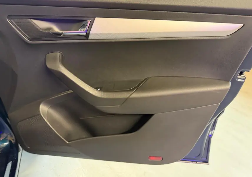 Vue rapprochée de la porte intérieure côté gauche d'une Skoda Karoq bleu, avec poignée chromée et rangements intégrés.
