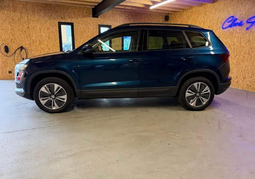 Vue latérale droite d'un Skoda Karoq bleu 2023 avec jantes alu 17 pouces et rampes de pavillon noires.