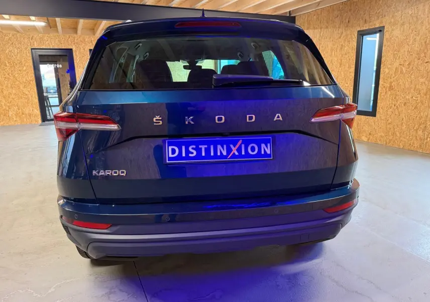 Vue arrière d'un Skoda Karoq bleu 2023 avec plaque Distinxion, feux LED et hayon électrique en intérieur showroom.