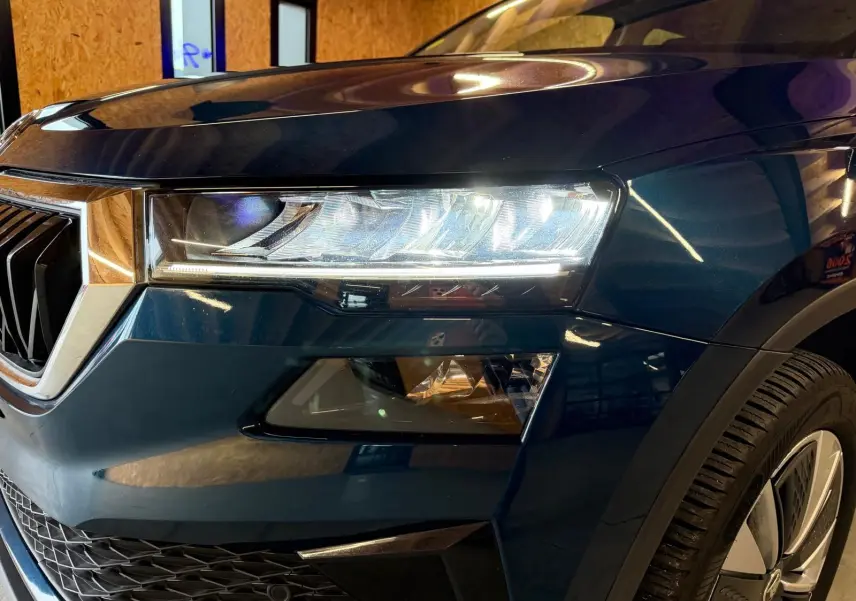 Gros plan sur l'avant droit bleu du Skoda Karoq 2.0 TDI 116 DSG7 Business avec phare LED et jante alu 17 pouces.
