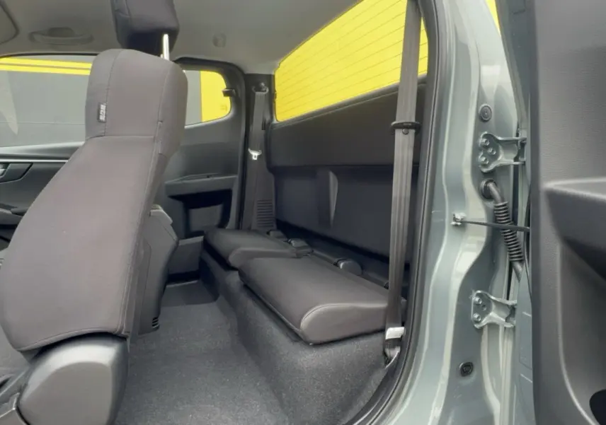 Vue intérieure arrière côté droit du pick-up Isuzu D-MAX 2.2 TD 164 Space Evolution avec sièges strapontins et peinture Inishmore green metallic visible.