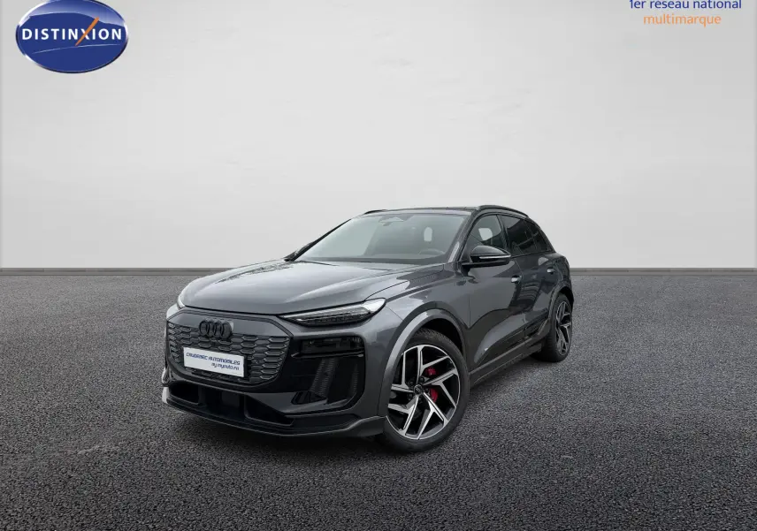 Audi Q6 e-tron gris nacré en 3/4 avant droit, avec jantes sport noires et étriers de frein rouges visibles.