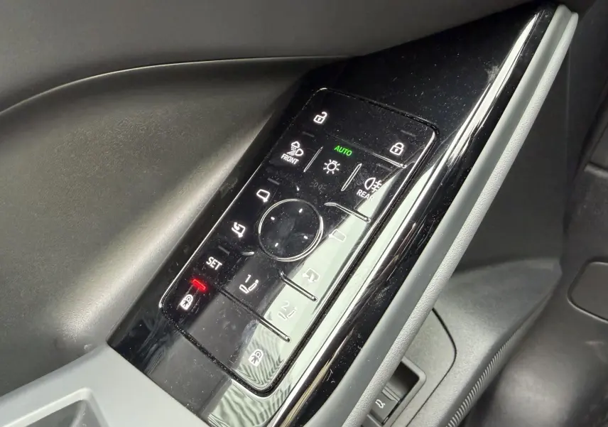 Panneau de commandes de porte côté conducteur de l'Audi Q6 e-tron 2024 avec finition noire brillante et boutons rétroéclairés.
