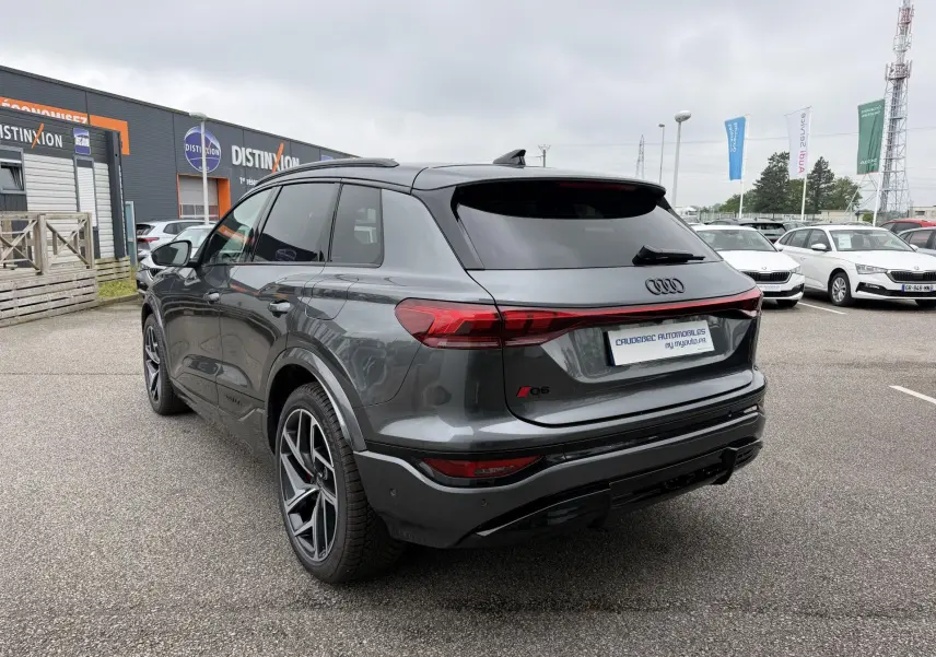 Audi Q6 e-tron gris nacré en 3/4 arrière droit, avec jantes sport noires et vitres arrière surteintées.