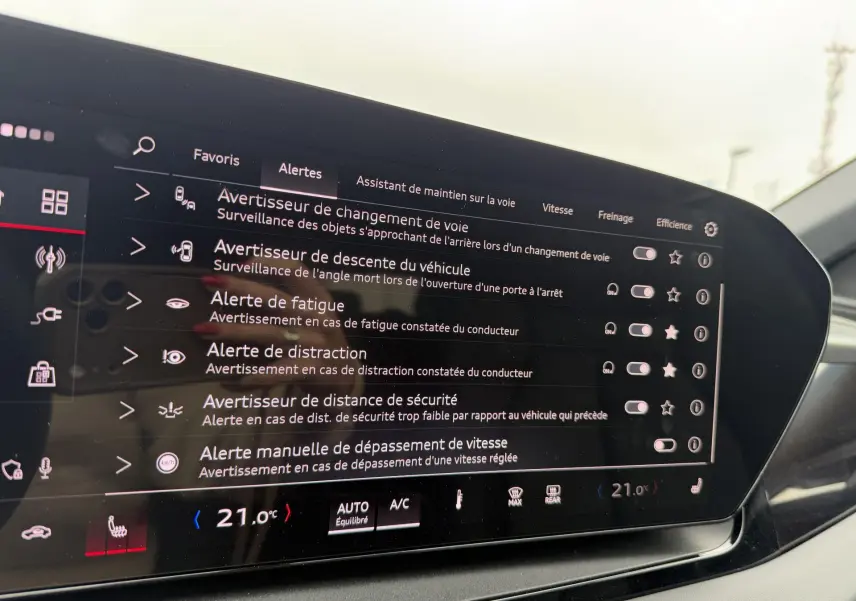 Écran tactile intérieur de l'Audi Q6 e-tron 2024 affichant les alertes de sécurité et la température à 21°C.