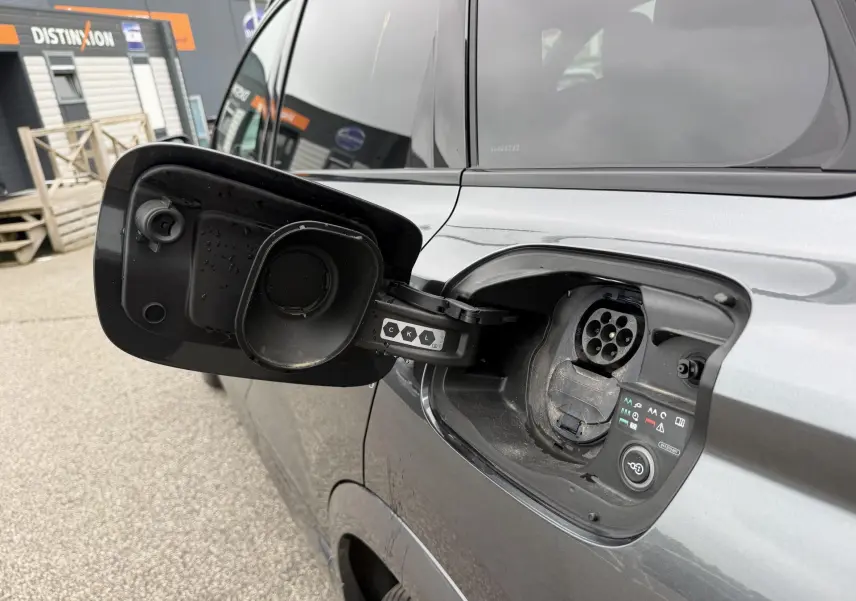 Prise de recharge ouverte côté gauche d’un Audi Q6 e-tron gris nacré, vue rapprochée sur la trappe électrique.
