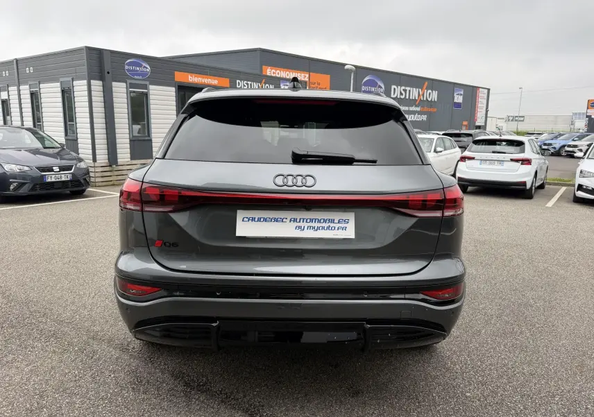 Vue arrière de l'Audi Q6 e-tron gris nacré avec feux arrière reliés et vitres arrière surteintées sur un parking.