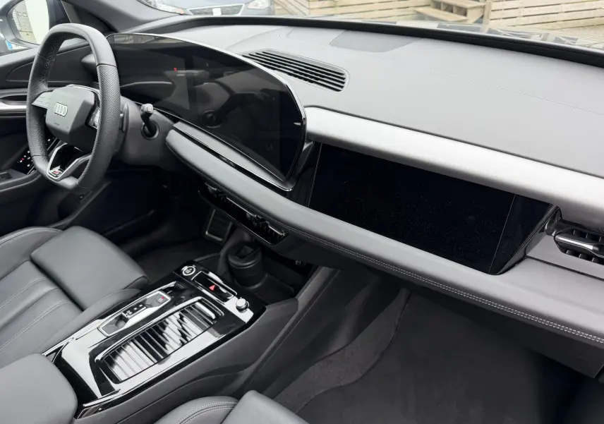 Vue intérieure côté conducteur de l'Audi Q6 e-tron 2024 avec tableau de bord noir et volant sport multifonction.