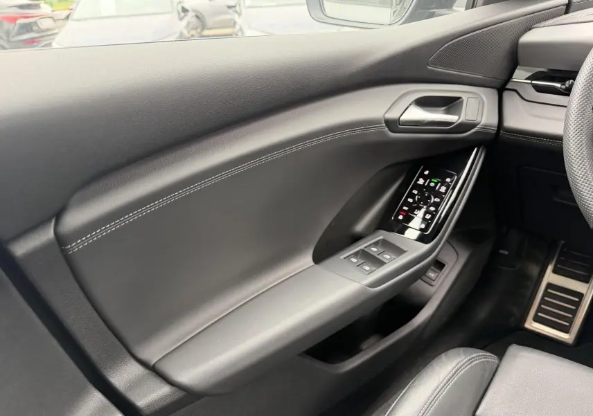 Intérieur côté conducteur de l’Audi Q6 e-tron 2024 en cuir noir avec commandes de vitres et pédalier acier inoxydable.