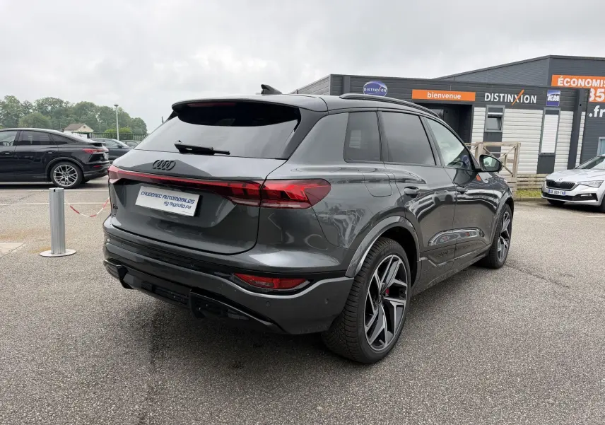 Audi Q6 e-tron gris nacré vu en 3/4 arrière droit, avec jantes Audi Sport noires et vitres surteintées.