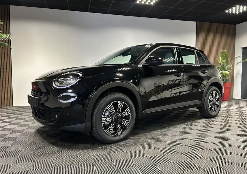 Vue 3/4 avant droite d'une FIAT 600 noire avec jantes alliage noires et détails chromés en intérieur showroom.