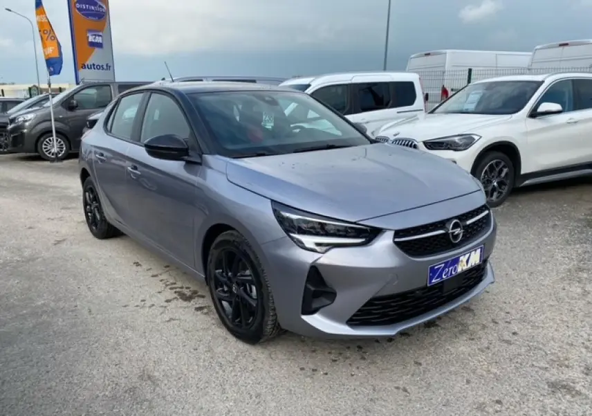 Opel Corsa gris magnetic vue 3/4 avant droit, jantes noires, toit noir et calandre distinctive sur parking.