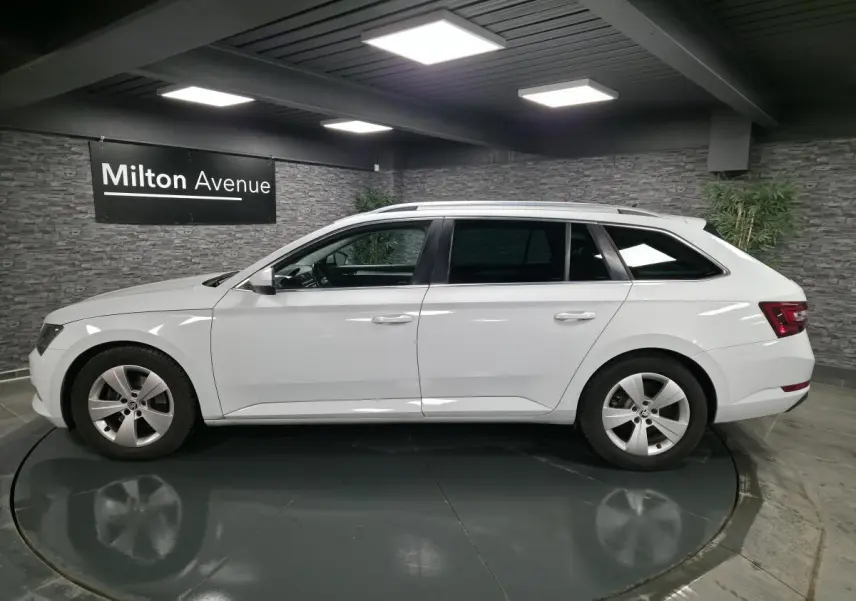 Vue de profil côté gauche d'un break SKODA SUPERB blanc avec jantes alliage 17 pouces dans un showroom.