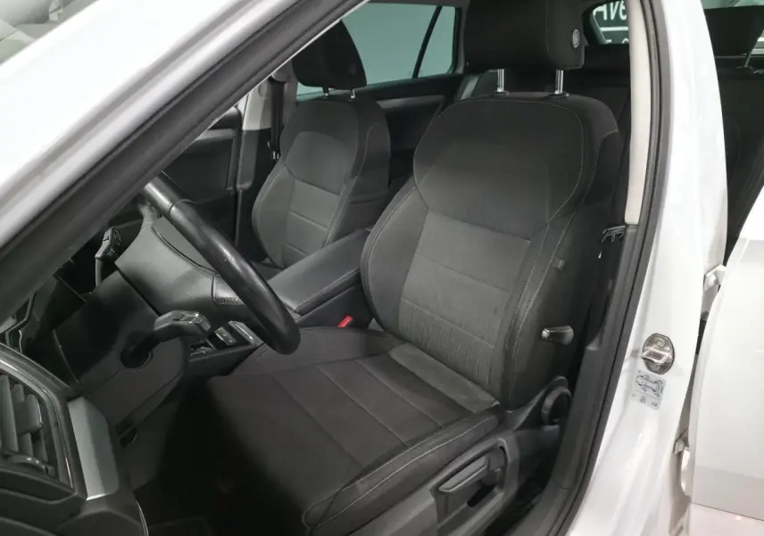 Vue intérieure côté conducteur de la Skoda Superb Combi blanche, sièges tissu noir et volant multifonctions en cuir.