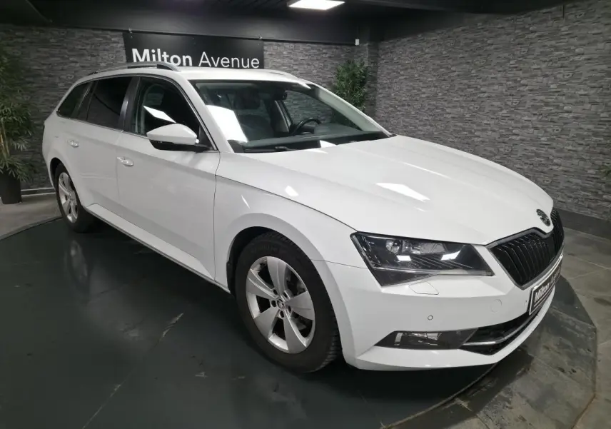 Vue 3/4 avant gauche d'un break Skoda Superb blanc avec jantes alliage 17 pouces dans un showroom.