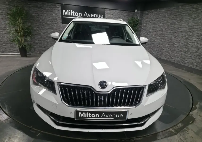 Vue avant d'une Skoda Superb Combi blanche avec calandre chromée et phares LED dans un showroom.