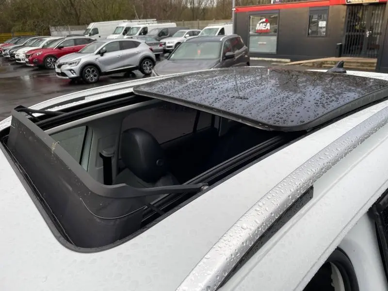 Vue rapprochée du toit ouvrant panoramique ouvert du Volkswagen Tiguan blanc pur, avec pluie visible sur le verre.