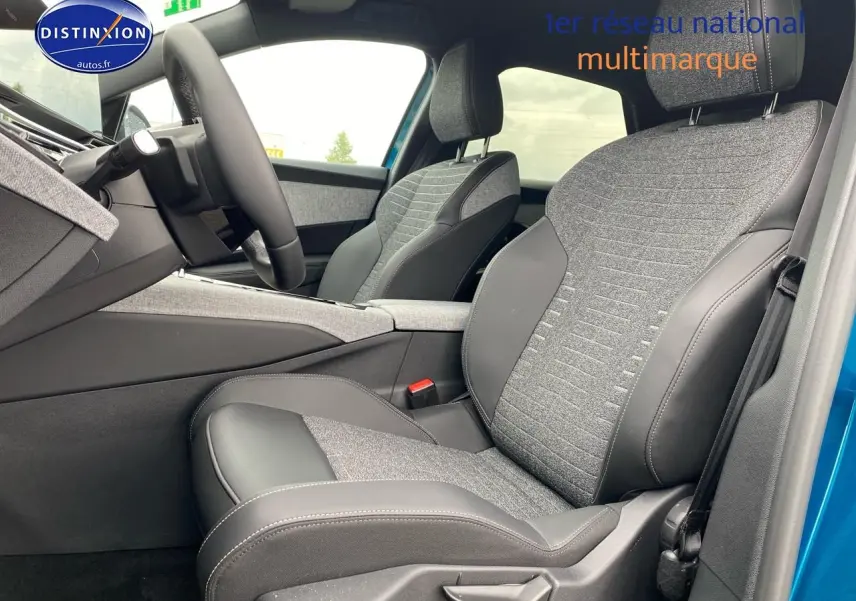 Vue intérieure côté conducteur du Peugeot 3008 bleu 2025, mettant en valeur les sièges tissu et cuir gris avec accoudoir central.