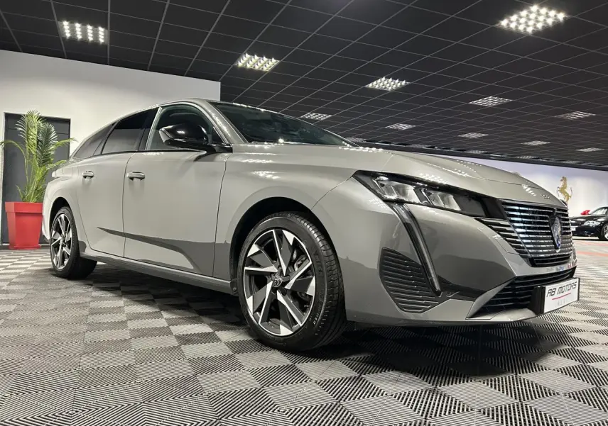 Peugeot 308 SW gris Sélénium vue 3/4 avant avec calandre noire et jantes alliage 17 pouces en intérieur showroom.