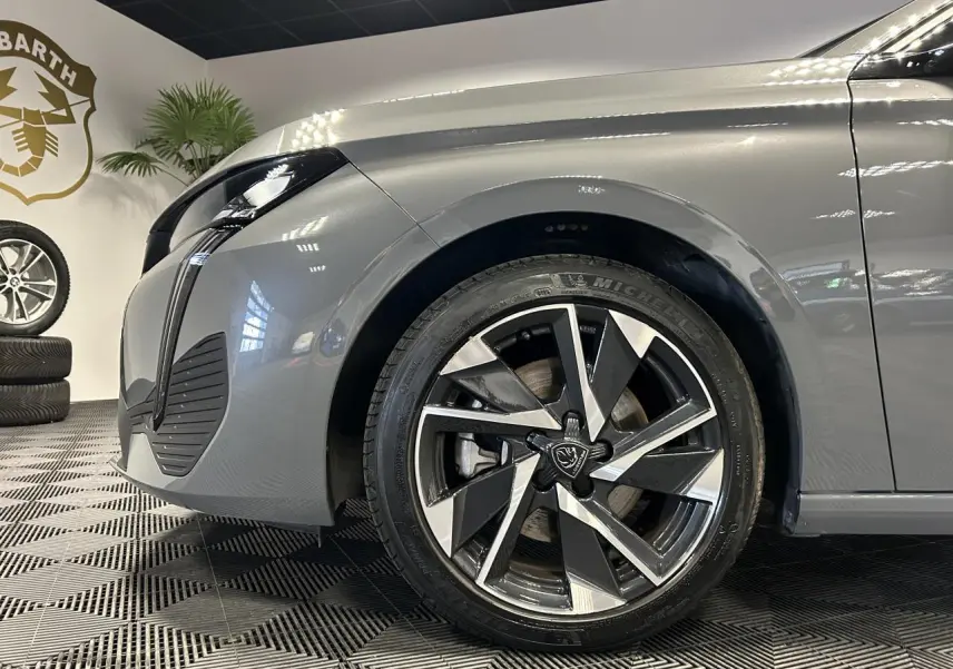 Gros plan sur la roue avant droite et l’aile avant gris Sélénium d’une Peugeot 308 SW hybride 2025 en showroom.