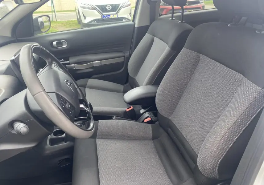 Intérieur avant de la Citroën C4 Cactus blanc, sièges gris avec accoudoir central et volant multifonction.