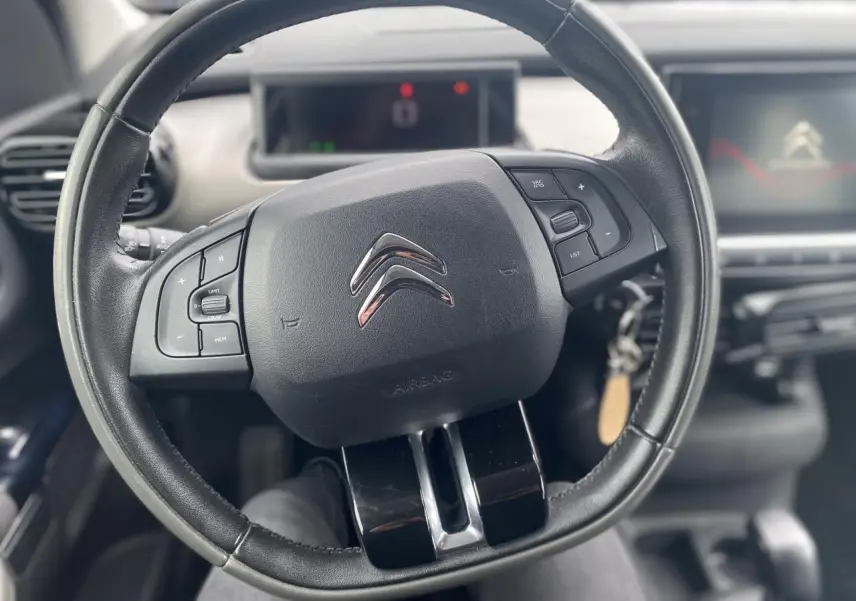 Vue rapprochée du volant noir de la Citroën C4 Cactus 2015 avec commandes intégrées et tableau de bord en arrière-plan.