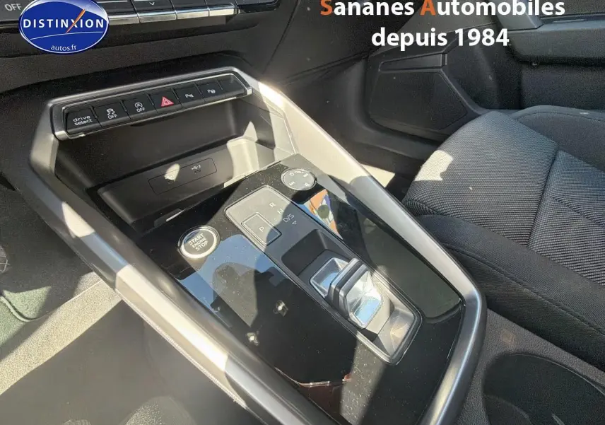 Vue rapprochée de la console centrale noire brillante de l'Audi A3 Sportback 2023 avec levier de boîte auto et boutons multifonctions.