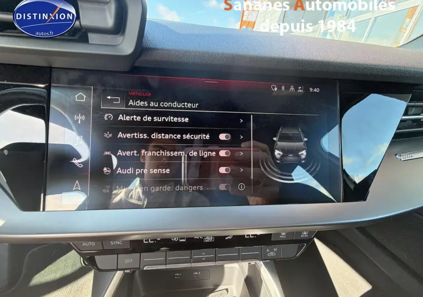 Écran tactile central affichant les aides à la conduite dans l’habitacle d’une Audi A3 Sportback blanche, vue de face.