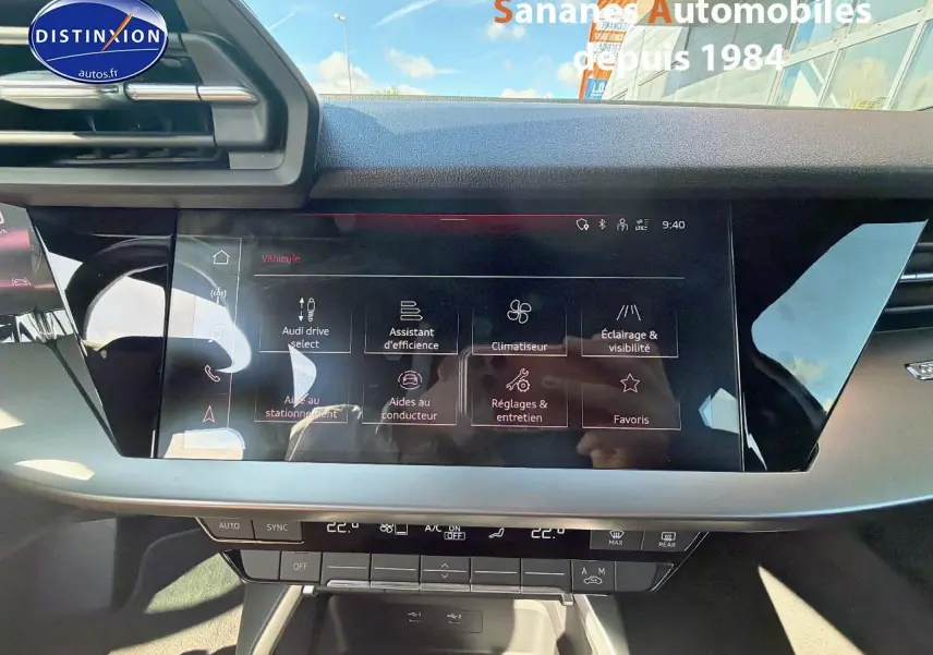 Vue rapprochée de l’écran tactile central noir brillant de l’Audi A3 Sportback blanc, affichant les options de conduite et confort.