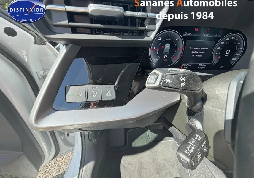 Vue intérieure côté conducteur de l'Audi A3 Sportback blanche 2023, montrant le tableau de bord digital et commandes au volant.