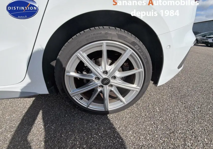 Gros plan sur la roue avant droite en alliage de l'Audi A3 Sportback blanche, avec jante S line visible.