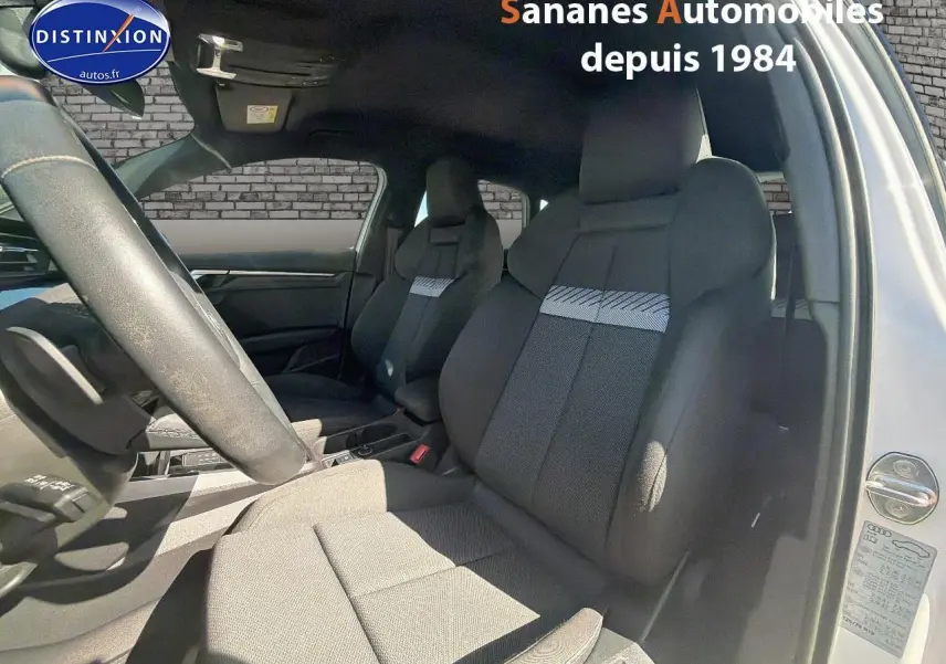Vue intérieure côté conducteur de l'Audi A3 Sportback blanche, mettant en valeur les sièges sport et le volant cuir multifonctions.