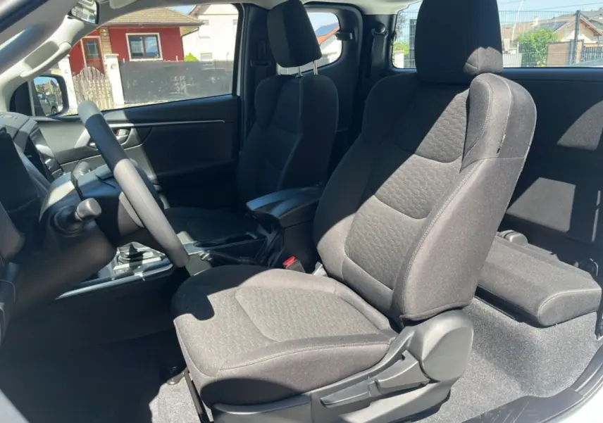 Vue intérieure côté conducteur du pick-up Isuzu D-MAX 2.2 TD 164 Space Evolution, sièges tissu gris et accoudoir central.