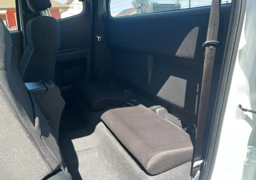 Vue intérieure côté droit du pick-up Isuzu D-MAX 2026 Splash white, montrant les strapontins arrière rabattus et sièges tissu noirs.