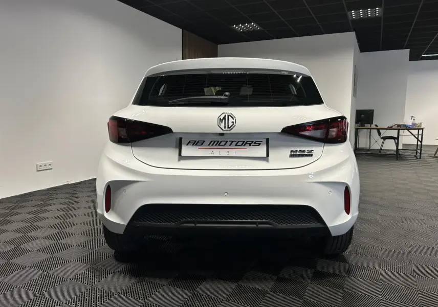 Vue arrière d'une MG3 1.5 Hybrid+ blanche 2025 en intérieur, avec feux arrière fumés et logo MG bien visible.
