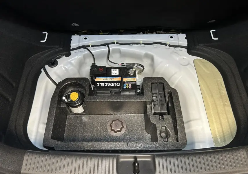 Vue plongeante sur le coffre ouvert d'une MG3 blanche, montrant la batterie et le rangement sous plancher.