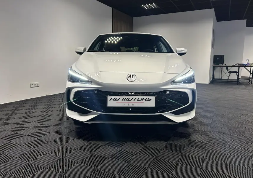 Vue frontale d'une MG3 blanche 2025 avec phares LED allumés dans un showroom moderne.