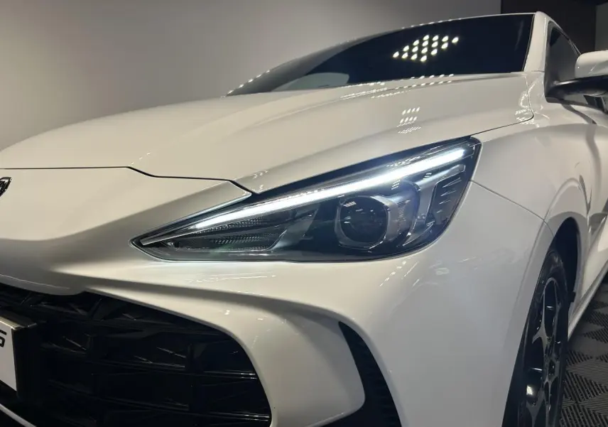 Vue 3/4 avant droit du MG3 blanc 2025 avec phares LED allumés et jantes alliage noires.