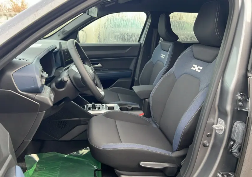 Intérieur côté conducteur du Dacia Duster 2025 noir nacré, sièges tissu avec logo HEV et tableau de bord moderne.