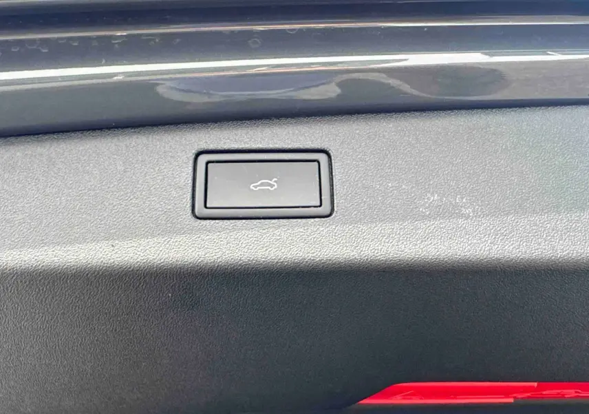 Bouton d'ouverture électrique du coffre sur la plage arrière d'un Volkswagen Tiguan gris, vue intérieure rapprochée.