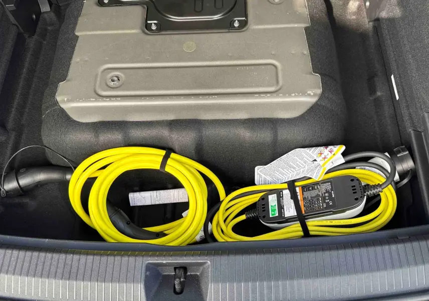 Coffre ouvert d’un Volkswagen Tiguan gris 2025 montrant un câble de recharge électrique jaune rangé.